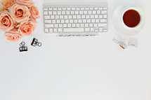 clips, computer keyboard, pencils, tea cup, and peach roses on a desk 