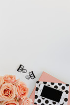journals, peach roses, phone, and clips on a white desk 