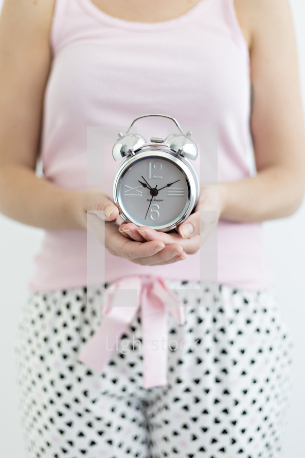 a woman in pjs holding an alarm clock 