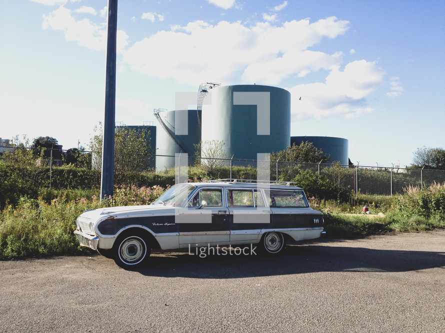 old station wagon parked in front of storage tanks 