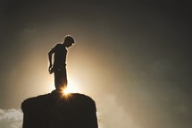 silhouette of a boy standing on a rock 