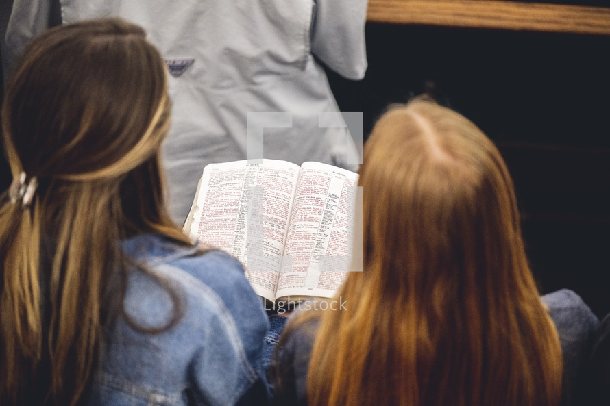 Two girls sharing the Bible and reading it during the church service.