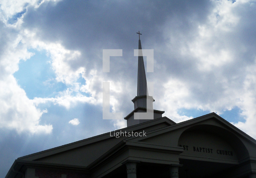 The exterior view of a Baptist church with church steeple against a stormy day surrounded by storm clouds