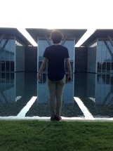 a man with his back to the camera standing in front of a reflection pool  