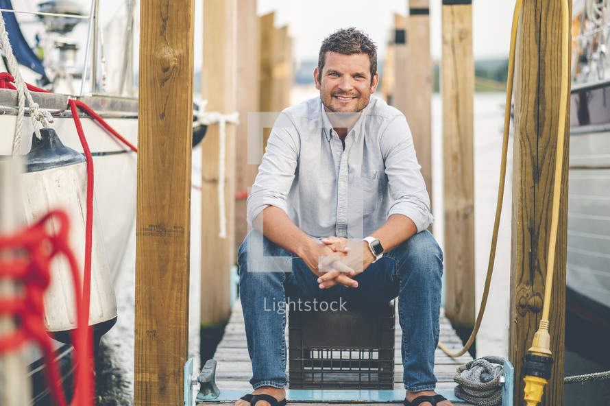 man sitting on a dock at a marina 