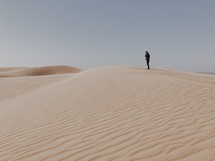 a man standing at the top of sand dunes 