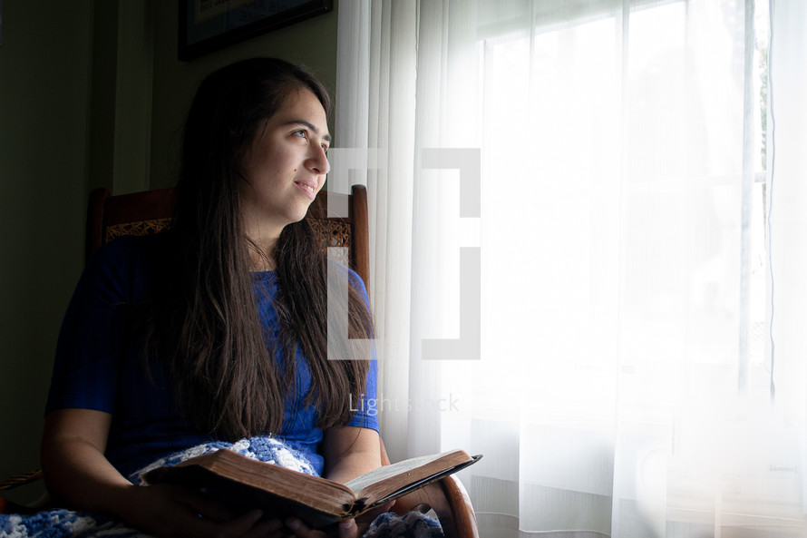 a woman sitting at a window reading a Bible 