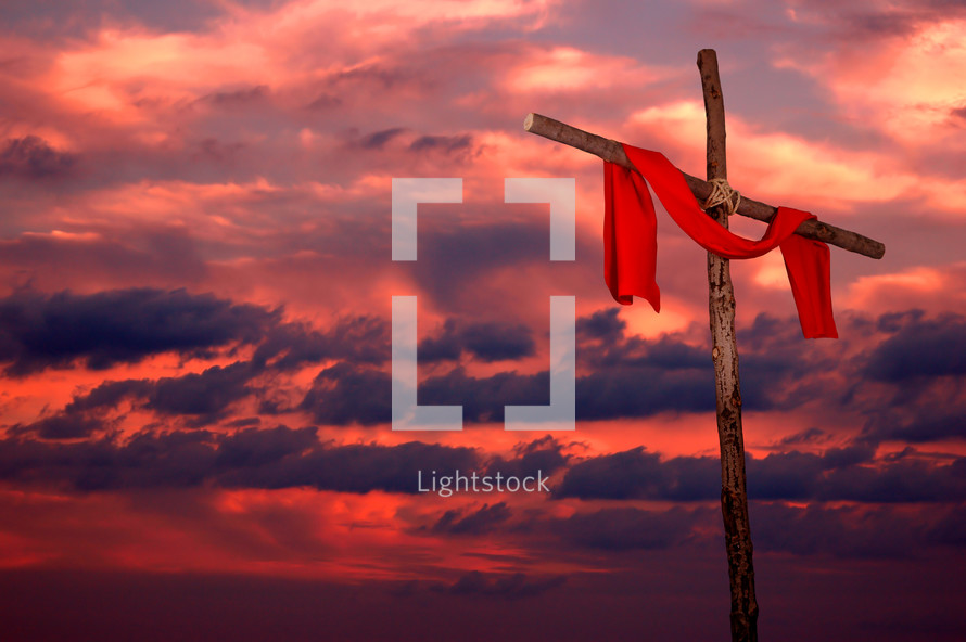 red tunic hanging on a wood cross against a fiery sky at sunset 