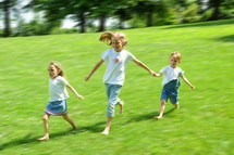 Three children running in a green field