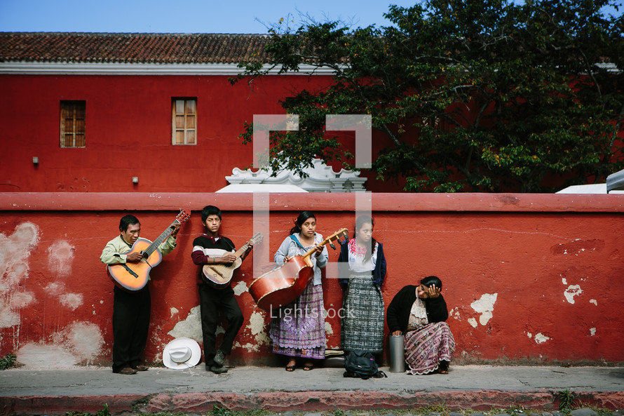 A mariachi band standing against a red stucco wall.