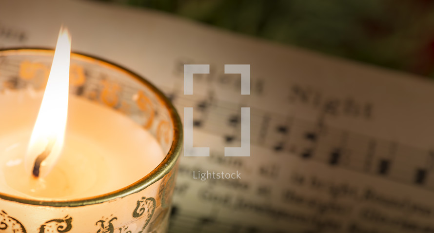 Lit candle om "Silent Night" sheet music.
