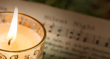 Lit candle om "Silent Night" sheet music.