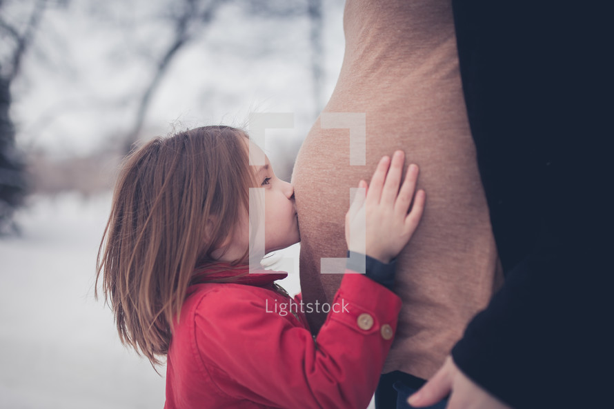 child kissing her mother's pregnant stomach 