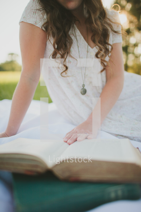 woman sitting on a blanket on the grass reading 