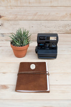 journal, polaroid camera, and house plant on a desk 
