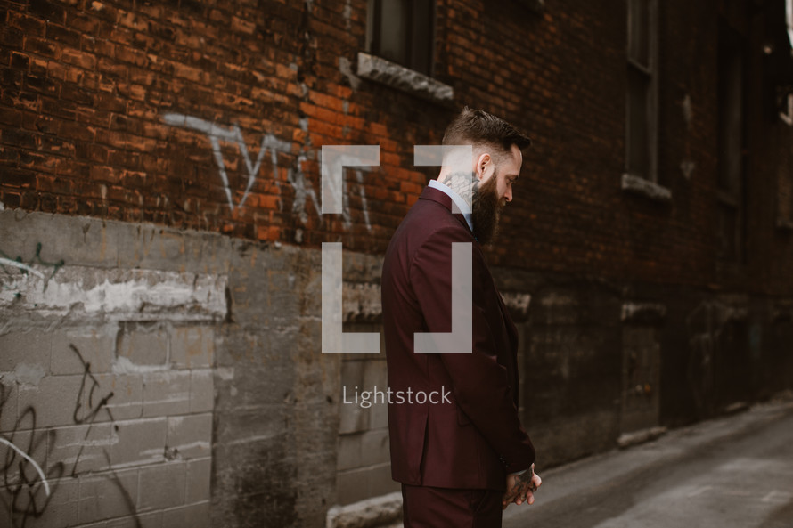 groom standing in an alley in front of a brick wall 