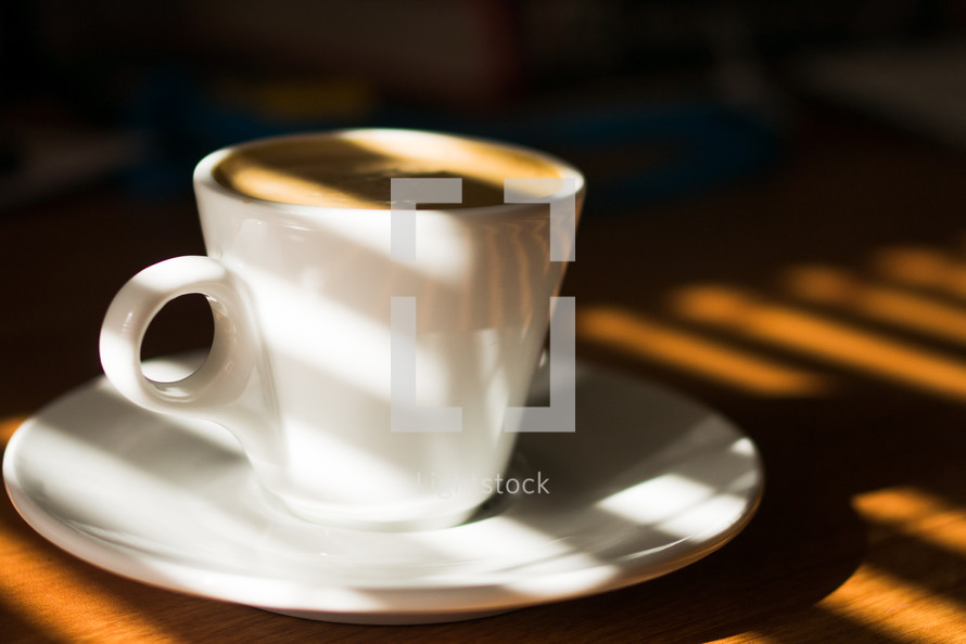 a cup of coffee in sunlight on a table 