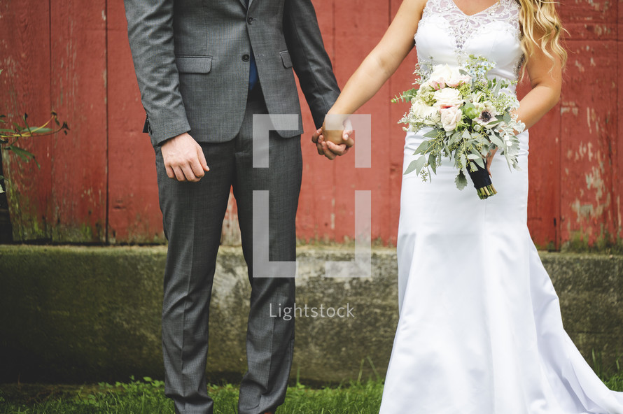 portrait of a bride and groom against a red barn 