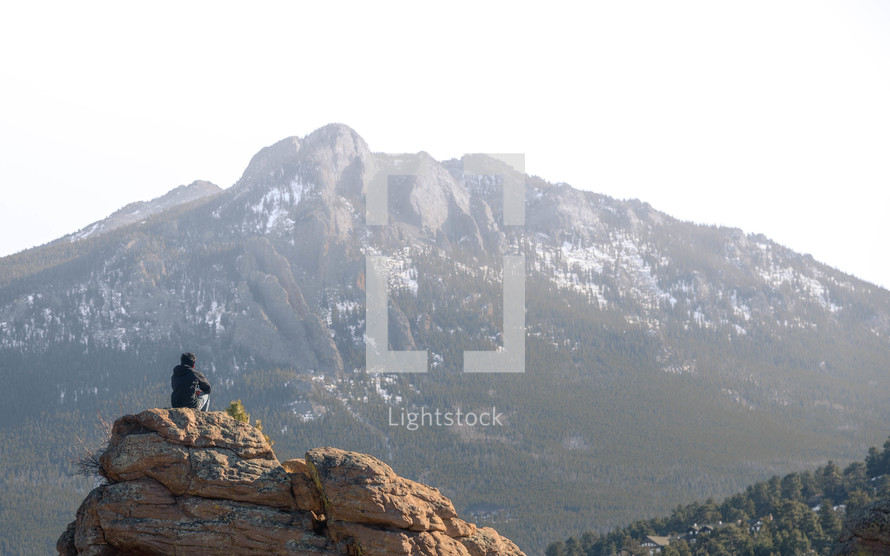 a man sitting on a rock looking up at a mountain 
