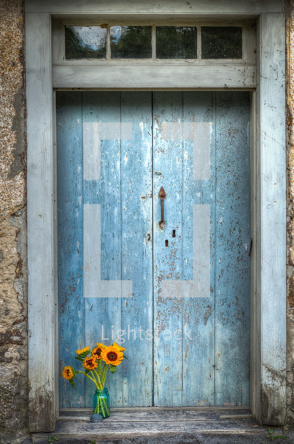 vase of sunflowers in front of a blue door 
