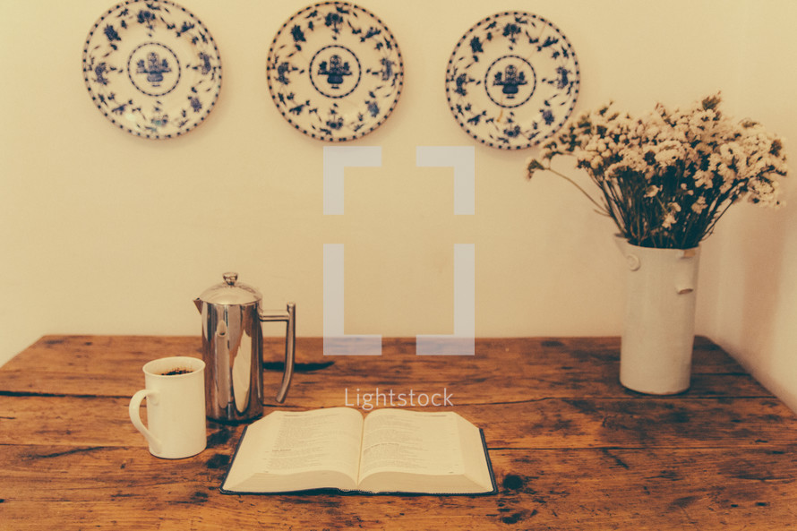 creamer, coffee mug, flowers in a vase and a Bible on a wood table 
