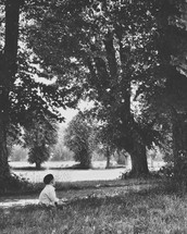 a child sitting in a park beside a pond 
