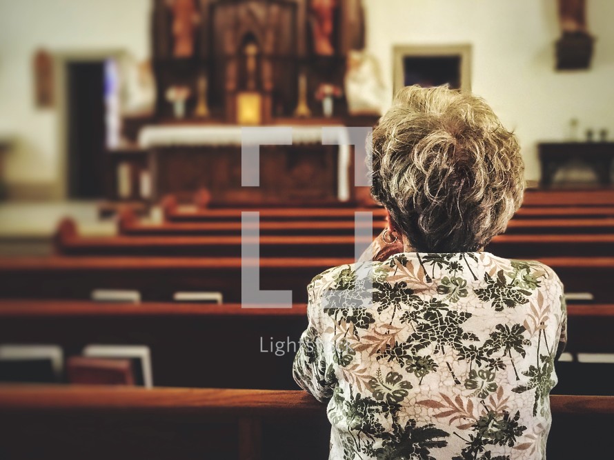 elderly woman praying alone in a church 
