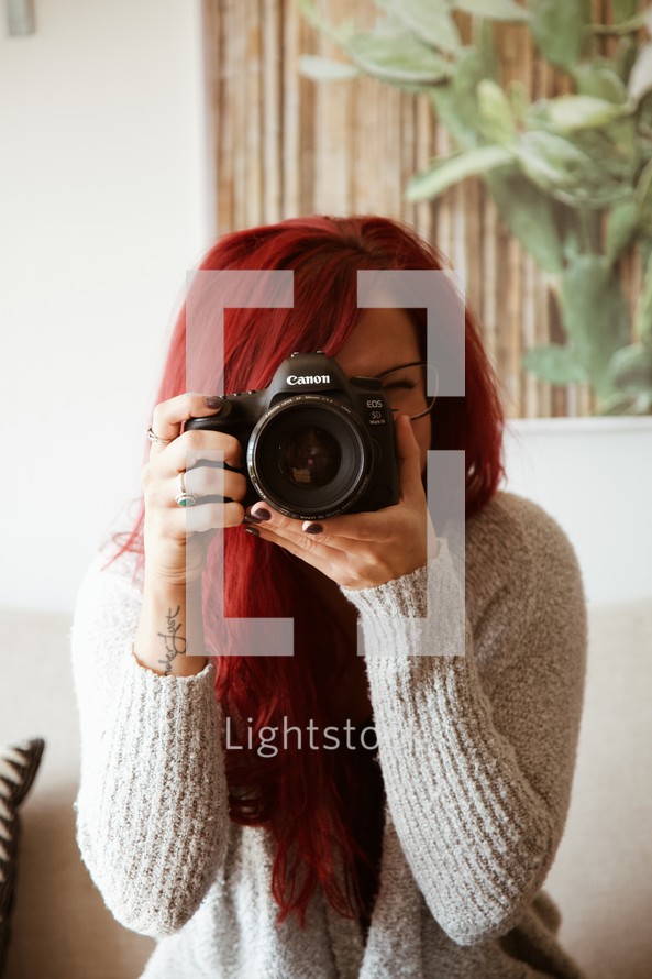 a woman with vibrant red hair holding a camera 