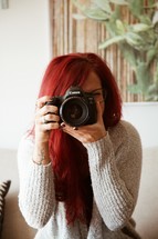 a woman with vibrant red hair holding a camera 