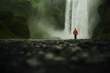 Low moody shot of Skogafoss with a man walking towards the waterfall with rocks in the foreground