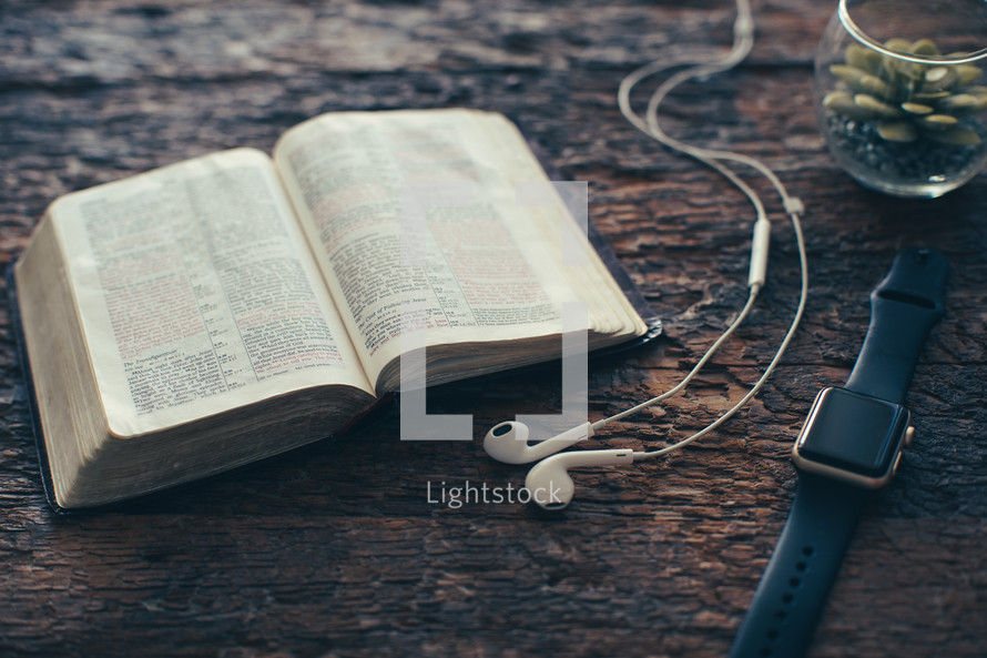 earbuds, open Bible, smartwatch, and houseplant on a wood background 