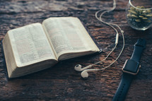 earbuds, open Bible, smartwatch, and houseplant on a wood background 
