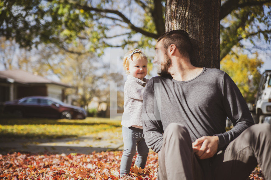 a father and little girl playing in fall leaves 