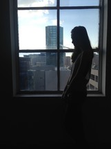 a sad woman standing in front of a window 