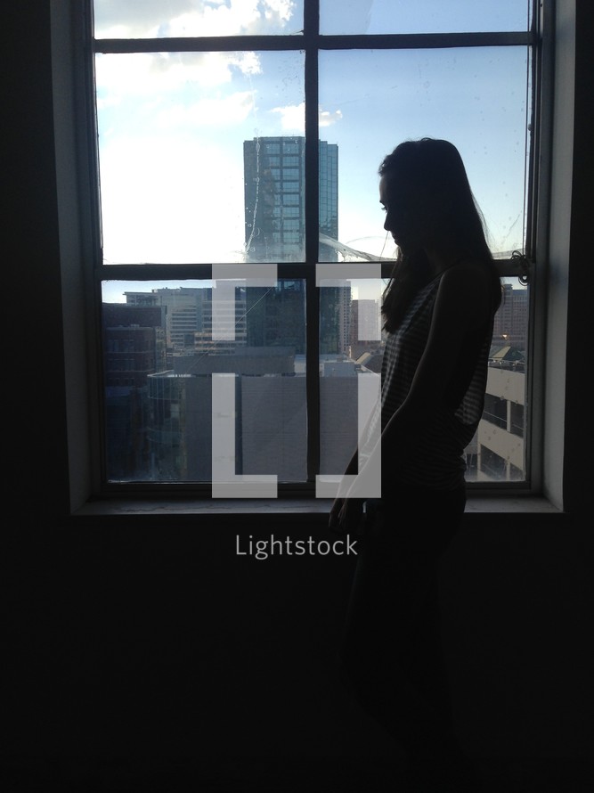 a sad woman standing in front of a window 