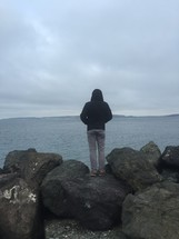 a man in a hoodie with his back to the camera standing on rocks 