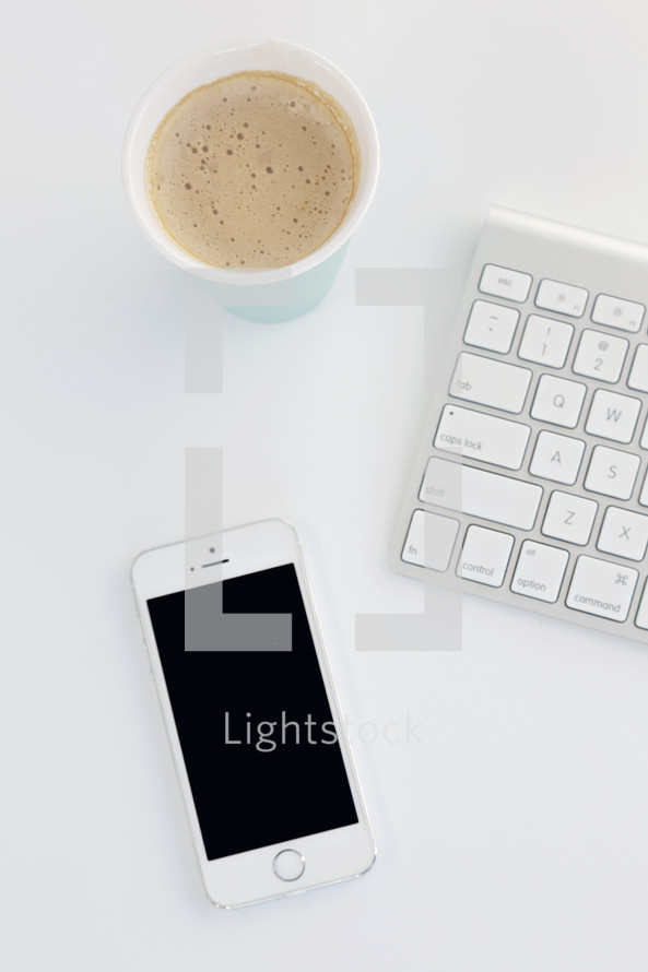 iPhone, latte, and computer keyboard on a white table 