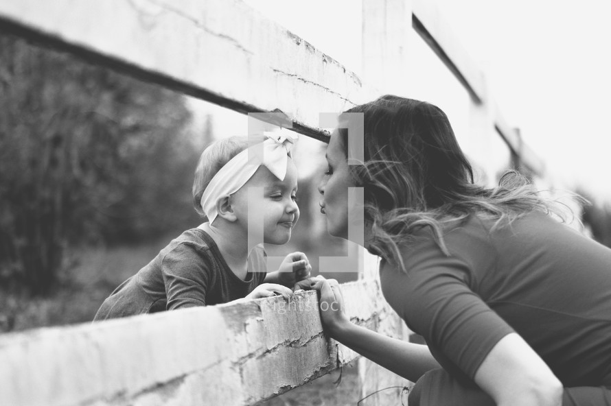 a mother kissing her toddler daughter through a fence 