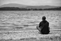 man sitting by a shore thinking 