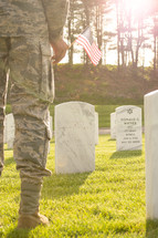 soldier holding an American flag standing in a cemetery 