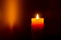 burning candle in dark with glow on wall