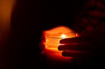 Hands holding glowing candle in dark