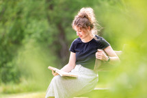 Woman smiling and reading Bible outdoors on bench