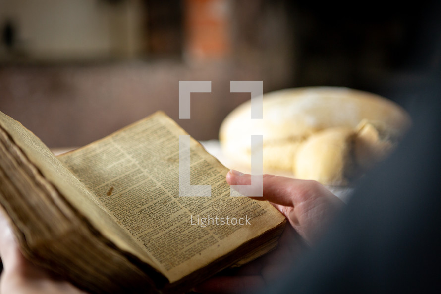 Closeup of person reading a Bible with bread in background