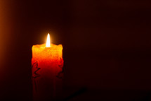 Solitary orange candle in dark
