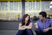 man holding out cash to a woman in front of a we buy gold store