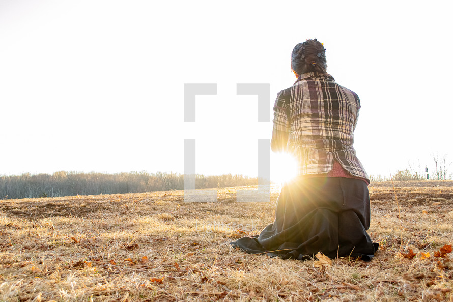 a woman kneeling in prayer in a field 
