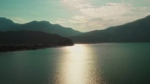 drone flies over big lake with mountains at golden hour