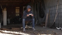 Young man, sad teenage boy anxious, depressed, sitting alone in a tool shed looking at a photograph.