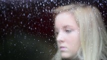 face of a teen girl behind wet glass 
